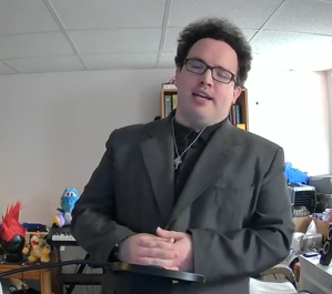 A screenshot of Earl from his April 30 2023 vlog, wearing business casual attire and a crucifix. In the background are toys and piles of boxes.